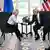 sentados, se dan la mano Trump y von der Leyen, el resto aplaude, de fondo, banderas.
