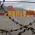 Yellow and red containers, most labeled MSC, are pictured piled up at a port in Cape Town, as seen through a barbed wire fence