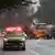 Several trucks and an emergency vehicle standing on a wet road