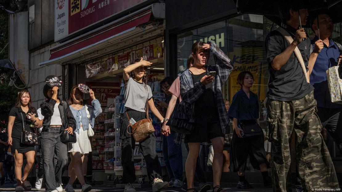 Pessoas protegem os olhos do sol enquanto caminham por uma rua em um dia quente em Tóquio Pessoas protegem os olhos do sol enquanto caminham por uma rua em um dia quente em Tóquio