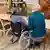 Una mujer, sentada a la mesa junto a otra mujer sentada en silla de ruedas.