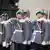 Soldaten in der grauen Uniformjacken und mit grünen Baretten präsentieren ihre Gewehre
