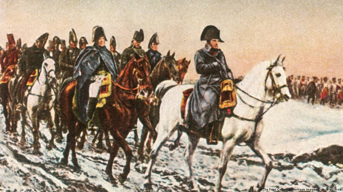 Картина, на которой изображена вереница конных всадников, впереди на белом коне - Наполеон Бонапарт в плаще Картина, на которой изображена вереница конных всадников, впереди на белом коне - Наполеон Бонапарт в плаще