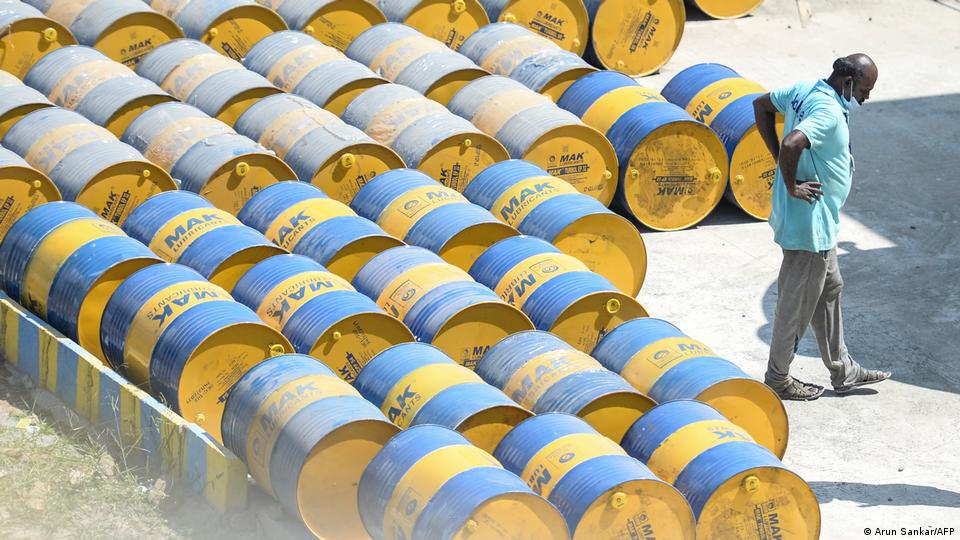 یک کارگر هندی در حال گذر از مقابل بشکههای نفت یک کارگر هندی در حال گذر از مقابل بشکههای نفت
