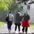 Three refugee women seen from the back, walking towards a fenced-in refugee home in Thuringia