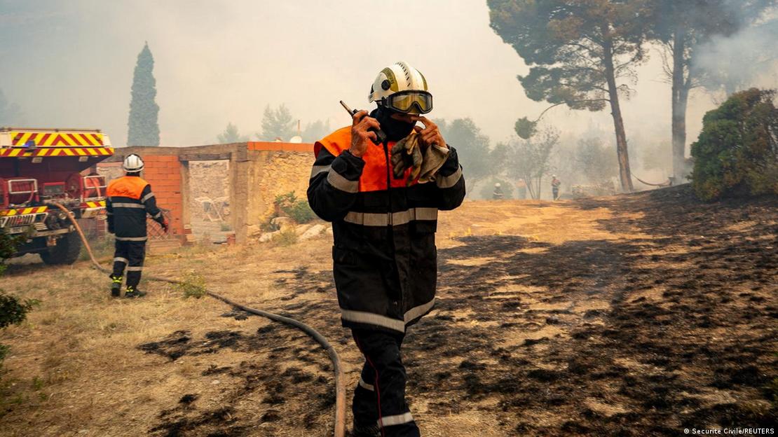 A firefighter wearing a helmut and goggles talks into a walkie-talkie in a scorched field near the village of Saint-Laurent-de-la-Cabrerisse, southern France, August 6, 2025.