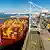 Ein Frachtschiff liegt im Hafen von Oakland und wird beladen, an Land warten viele Container