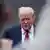O presidente dos Estados Unidos, Donald Trump, caminha enquanto olha para baixo de maneira séria. Ele veste camisa clara e gravata e terno escuro.