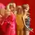 A blonde doll wears a black and white striped swimsuit and topknot ponytail, while other dolls are blurred in the background.