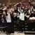 A young orchestra plays and some members hold up their arms