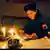 A woman (Nerxhivane Azizi) in a military hat and uniform with a badge marked UCK (Kosovo Liberation Army) on the sleeve reads a newspaper by candlelight