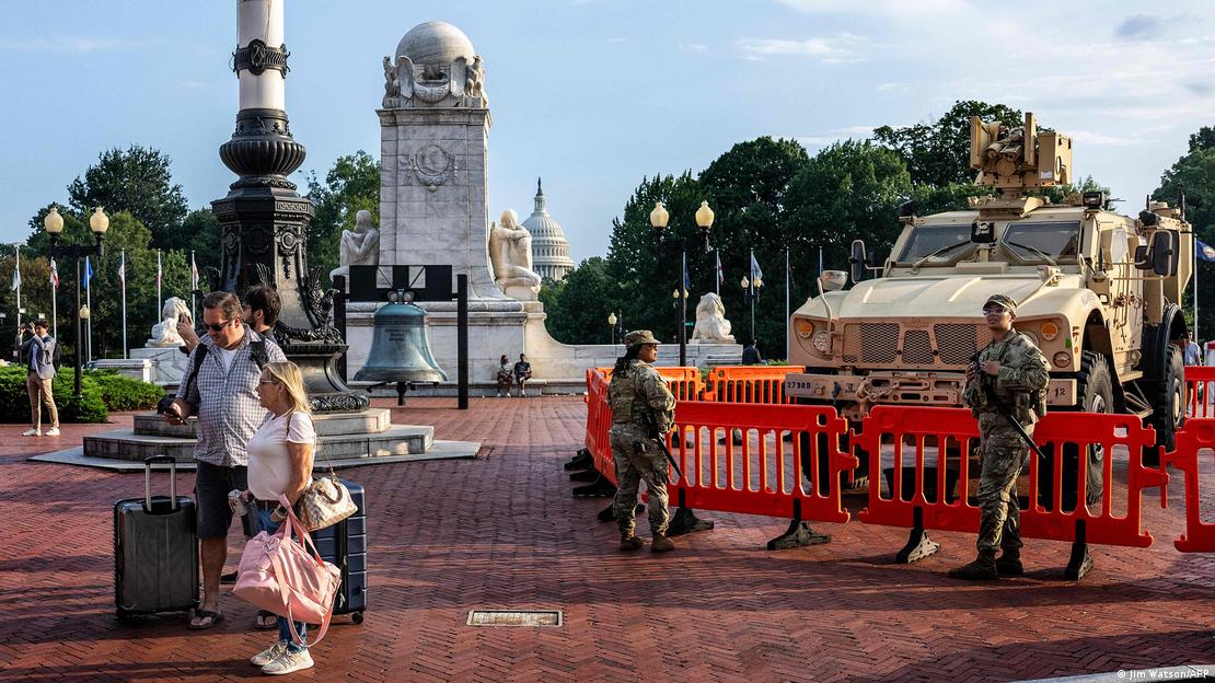 Reisende mit Gepäck gehen an Mitgliedern der Nationalgarde vorbei