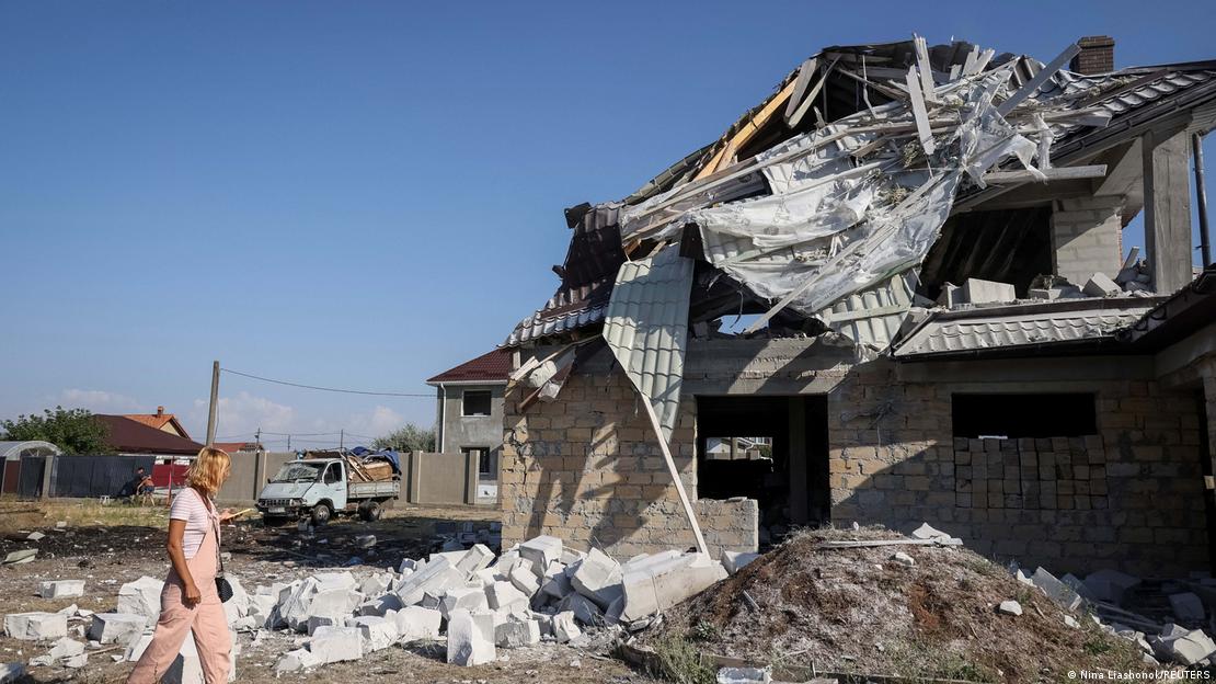Eine Frau geht auf ein schwer beschädigtes Haus zu