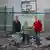 Drei Menschen stehen in einer zerstörten Turnhalle und blicken in eine Kamera