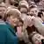 Almanya Başkanı Merkel, etrafında çok sayıda çocukla selfie yaparken, yeşil ceketli Merkel kameralara tebessüm ediyor