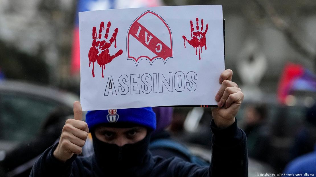 hombre sostiene cartes con dibujo de manos ensangrentadas, escudo del club Independiente y la palabra "asesinos".