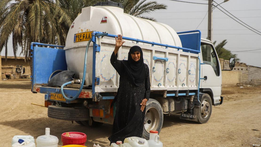 A woman in burqa waves while standing next to a small truck transporting water A woman in burqa waves while standing next to a small truck transporting water