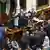 El político habla en pie desde la mesa del Senado mientras un grupo de legisladores se agolpa enfrente de él también de pie.