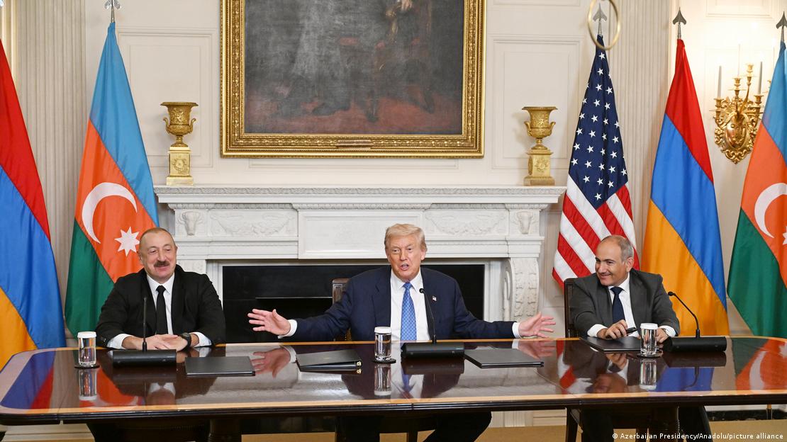 U.S. President Donald Trump gestures widely as he sits between Azerbaijani President Ilham Aliyev and Armenian Prime Minister Nikol Pashinyan in front of their respective flags