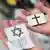 Symbolbild Christentum und Judentum: Zwei Hände, in einer eine Karte mit einem Kreuz, in der anderen Hand zwei Karten mit Davidstern und Menora