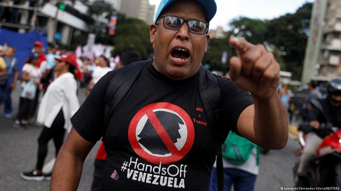 Un hombre con una camiseta que dice "Hands Off Venezuela" grita ante la cámara. Un hombre con una camiseta que dice "Hands Off Venezuela" grita ante la cámara.