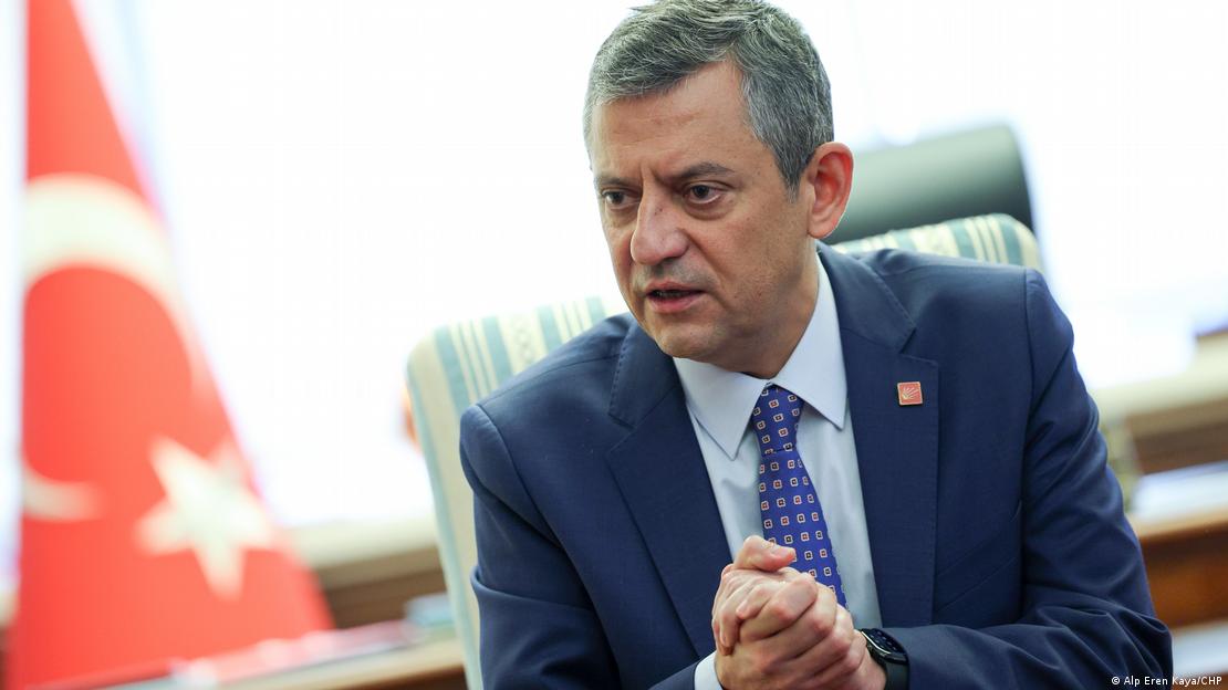 CHP Genel Başkanı Özgür Özel, fonda Türk bayrağının bir masada iki elini birbirine kavuşturmuş şekilde konuşuyor. 