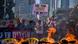 Manifestantes atrás de barricada em chamas protestam bloqueando avenida e pedindo libertação dos reféns; mulher segura cartaz com dizeres "podemos salvar o restante"