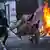 Manifestantes en Yakarta, con mascarilla y pañuelo tapando sus rostros. Uno lleva un mueble de madera en sus manos, al pasar junto a la puerta de un edificio incendiada. (31.08.2025).