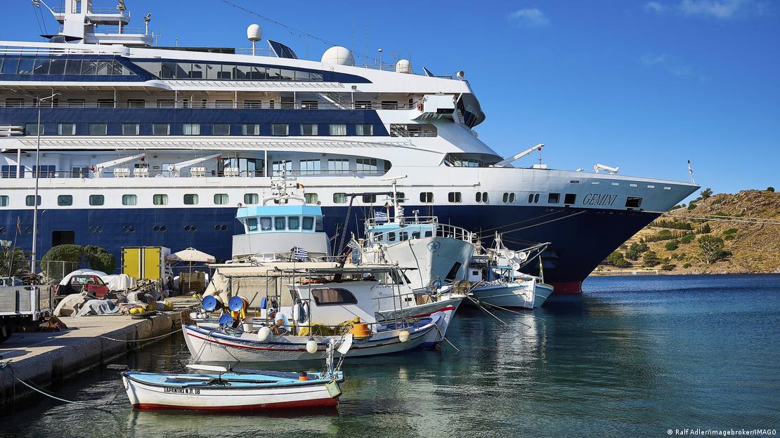 İskeleye yanaşmış bir yolcu gemisinin ön kısmı. Geminin yanında daha ufak boyutlu balıkçı tekneleri bulunuyor