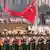 Ein Offizier hisst die chinesische Flagge, während ein Musikkorps vor Zuschauertribünen marschiert