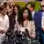 Lisa Phillips habla ante los micrófonos de la prensa con muchas mujeres y algunos hombres detrás de ella.