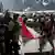 A woman waves an Indonesian flag in the direction of riot police officers, during a clash at a protest against what the demonstrators say are exorbitant allowances for Indonesian parliament members, outside Indonesian parliament buildings, in Jakarta