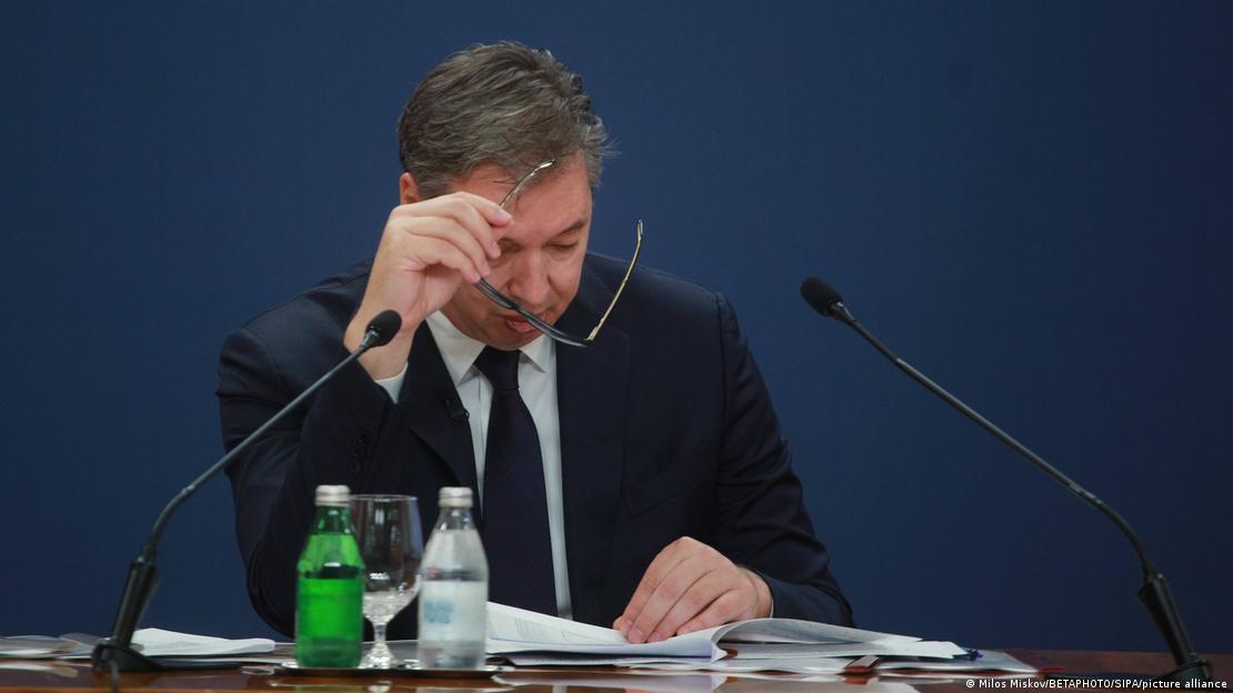 Маж со темен костум и очила в рака (претседателот на Србија, Александар Вучиќ) гледа во документи додека дава изјава во Палатата на Србија