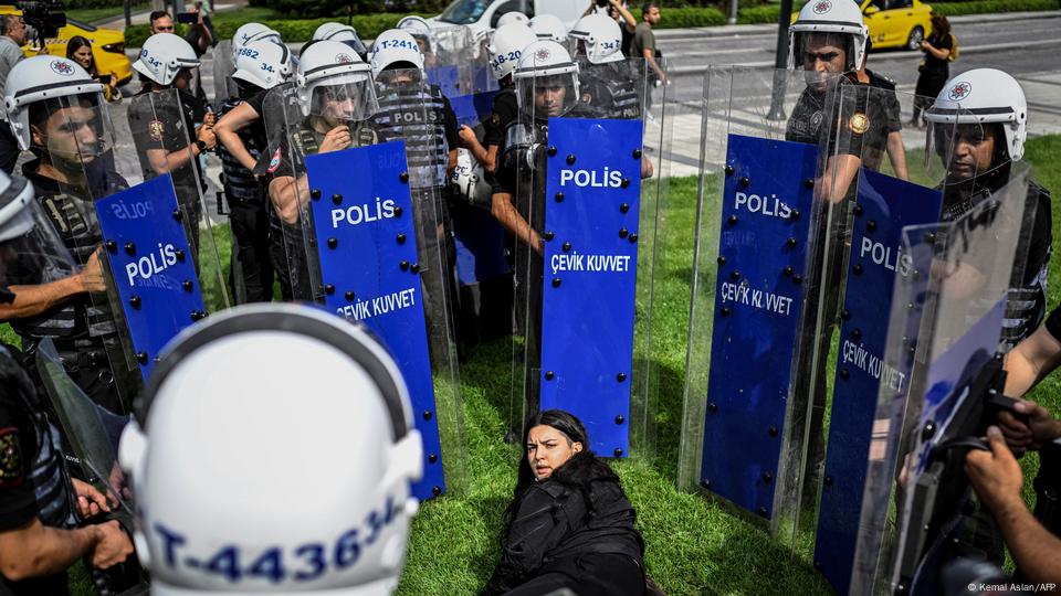 Polis kalkanlarıyla çember içine alınmış genç bir kadın yerde duruyor