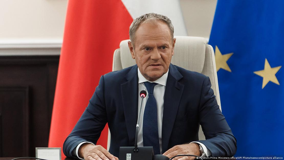 Der polnische Regierungschef Donald Tusk sitzen an einem Tisch mit einem eingeschalteten Tischmikrofon, hinter ihm die polnische Fahne und die EU-Flagge