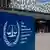 A woman walks besides the entrance to the ICC with a logo of the court in the forefront.