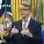 Donald Trump (seated, frowning) with Peter Mandelson, spectacled man, standing and speaking
