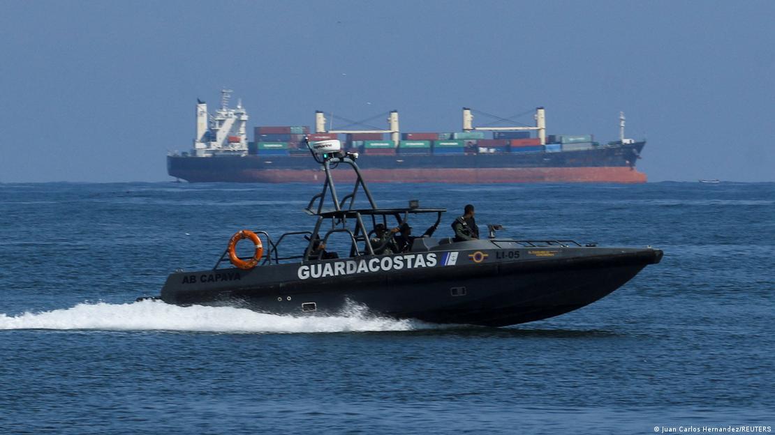 Una lancha con el texto "guardacostas" a un costado avanza frente a un buque.