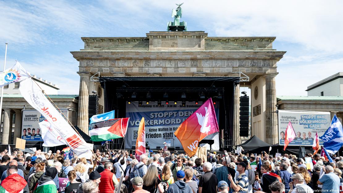 "Stoppt den Völkermord in Gaza!" steht auf einem riesigen Transparent, das auf einer Bühne direkt vor dem Brandenburger Tor in Berlin platziert ist. Davor haben sich über 10.000 Menschen zu einer Kundgebung versammelt. Manche schwenken Fahnen mit der Friedenstaube oder der Palästina-Fahne in den Farben Schwarz, Weiß, Grün und Rot.   