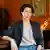 Author Ayelet Gundar-Goshen sits in a room with paintings behind her