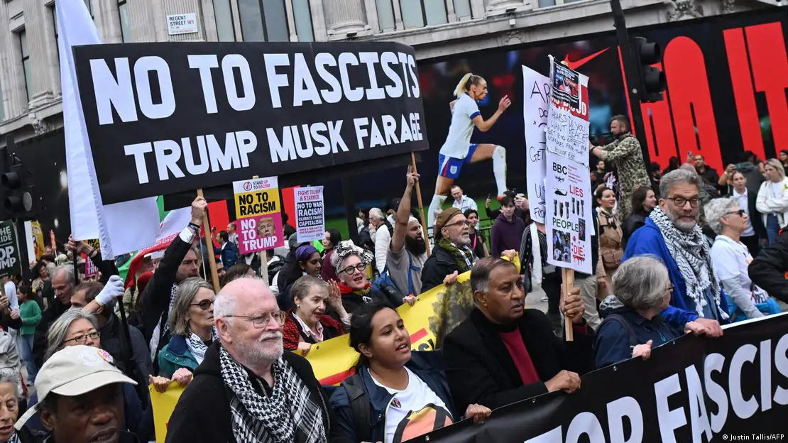 Un grupo de personas portan varias pancartas y corean eslóganes. En una de ellas se lee "No a los fascistas", junto a los nombres de Trump, Musk y Farage.