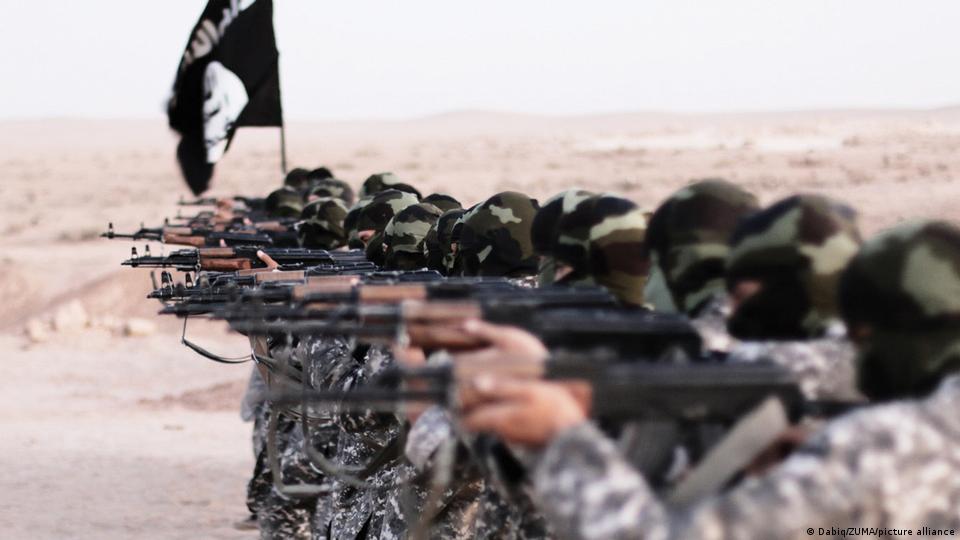 داعش کی ایک پروپیگنڈا ویڈیو سے لی گئی ایک تصویر، نومبر 2015ء: شامی شہر رقعہ میں تربیت، داعش کا جھنڈا اور اس تنظیم کے مسلح، نقاب پوش عسکریت پسند داعش کی ایک پروپیگنڈا ویڈیو سے لی گئی ایک تصویر، نومبر 2015ء: شامی شہر رقعہ میں تربیت، داعش کا جھنڈا اور اس تنظیم کے مسلح، نقاب پوش عسکریت پسند