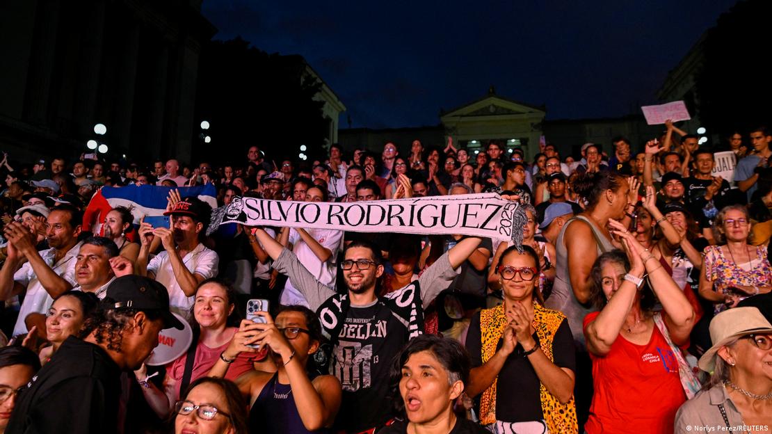 Un espectador muestra una bufanda con el nombre de Silvio Rodríguez entre una multutid de publico con banderas y otras pancartas.