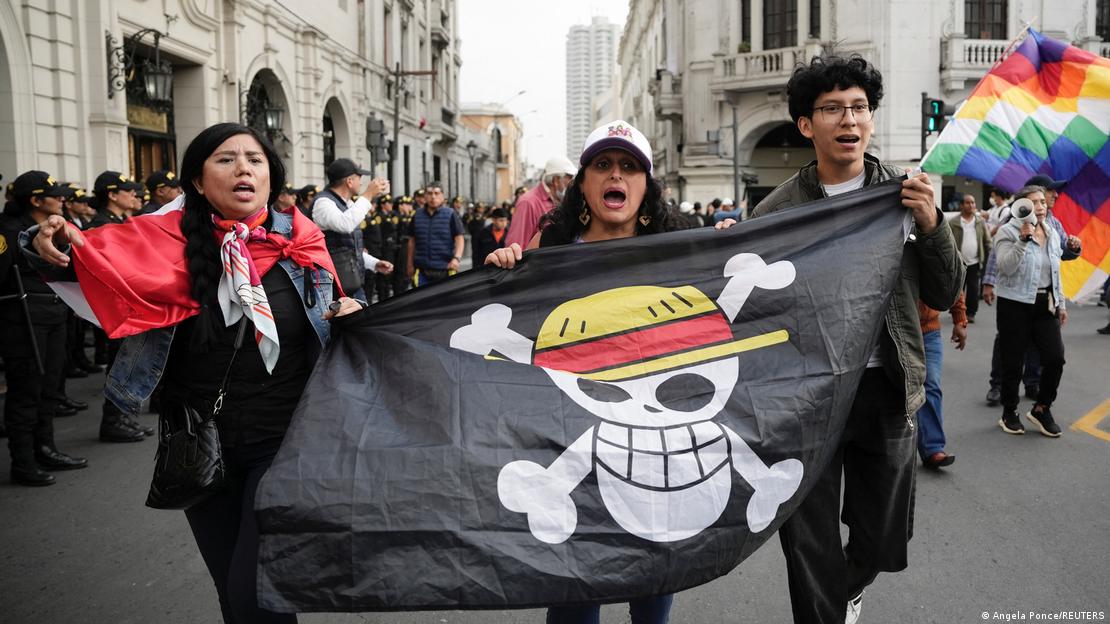 Perú, Lima | Tres jóvenes con una bandera negra que muestra una calavera sonriente con un sombrero de paja, en una manifestación contra la presidenta Dina Boluarte. Perú, Lima | Tres jóvenes con una bandera negra que muestra una calavera sonriente con un sombrero de paja, en una manifestación contra la presidenta Dina Boluarte.