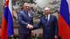 Slovakya Başbakanı Robert Fico ile Rusya Devlet Başkanı Vladimir Putin gülümseyerek tokalaşıyor, arka planda her iki ülkenin bayrakları