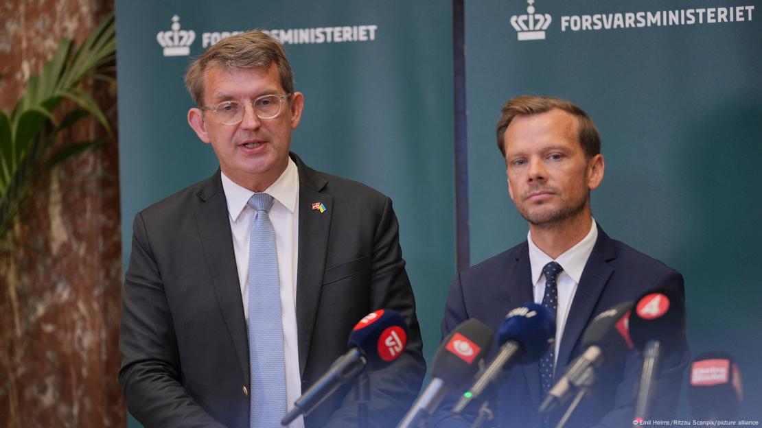 O ministro da Defesa da Dinamarca, Troels Lund Poulsen, e o da Justiça, Peter Hummelgaard, falam em frente a vários microfones durante entrevista coletiva de imprensa em Copenhague. Eles vestem ternos escuros e camisas claras.