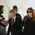 O ex-presidente da França, Nicolas Sarkozy, deixa a corte em Paris ao lado da mulher, Carla Bruni-Sarkozy. Ao fundo, é possível ver policiais franceses. Carla está de vestido escuro e óculos de sol. Sarkozy veste terno e gravata escuros e camisa branca.