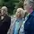 Four older persons look quizically in the distance while standing outside amid trees.