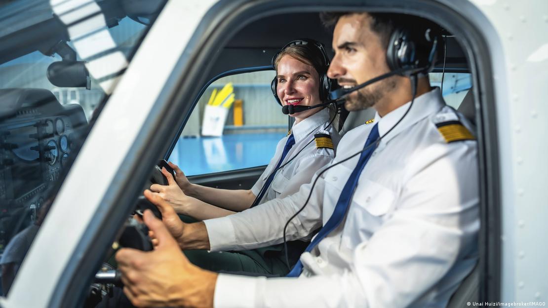  Kulaklıklı ve gülümseyen erkek ve kadın pilotlar, hangarda küçük bir uçağı kontrol ediyor ve havacılığın ruhunu temsil ediyor 