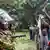 Demonstranten (r.) diskutieren mit Polizisten (l.) während einer Protestaktion auf einer Wiese vor einem Gebäude (in Nairobi, Kenia im Juni 2025)